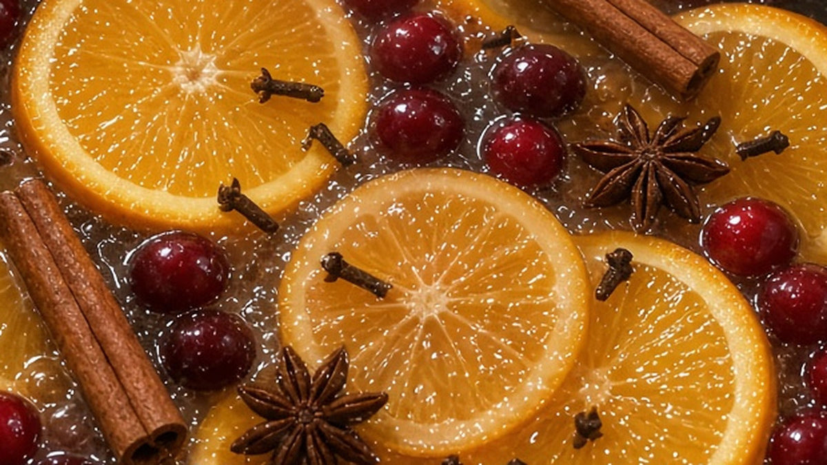Close-up of a stovetop simmer pot: orange slices, fresh cranberries, cinnamon sticks, whole cloves and star anise simmering in water.