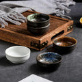 Blue speckled pinch bowl in front, with white, rust and green-speckled bowls beside a wood serving tray
