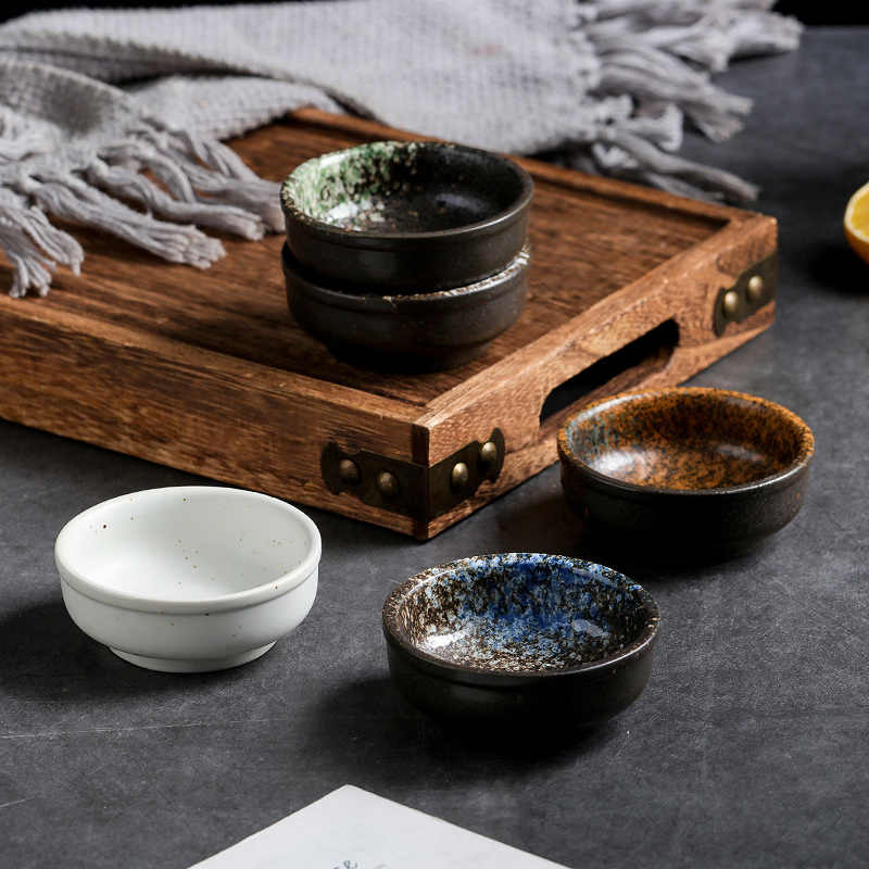 Blue speckled pinch bowl in front, with white, rust and green-speckled bowls beside a wood serving tray