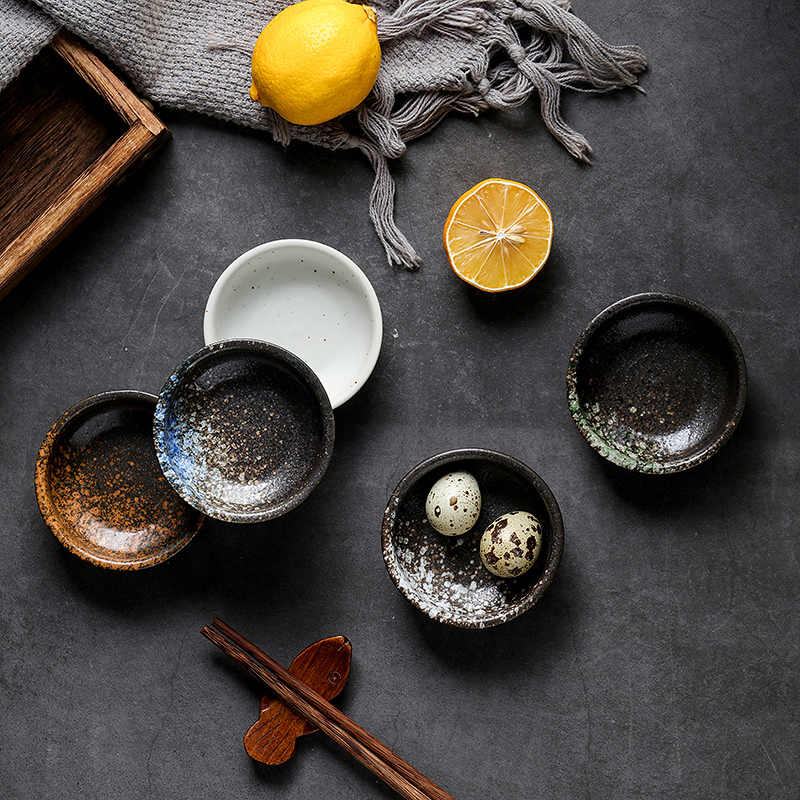 Overhead view of a blue speckled pinch bowl beside white, rust, green-speckled and white-speckled bowls, one holding quail eggs, with lemons and chopsticks