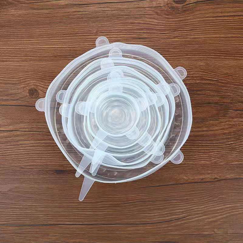 Six clear silicone stretch lids in graduated sizes nested on a wood table