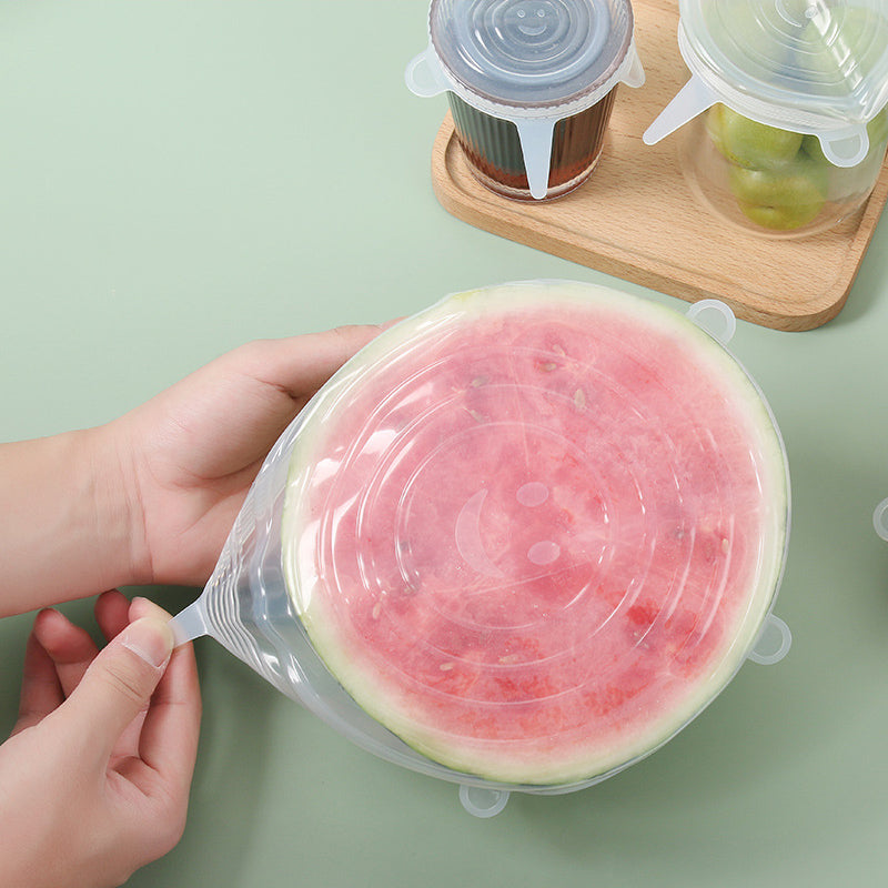 Hands stretching a clear silicone lid over a cut watermelon half